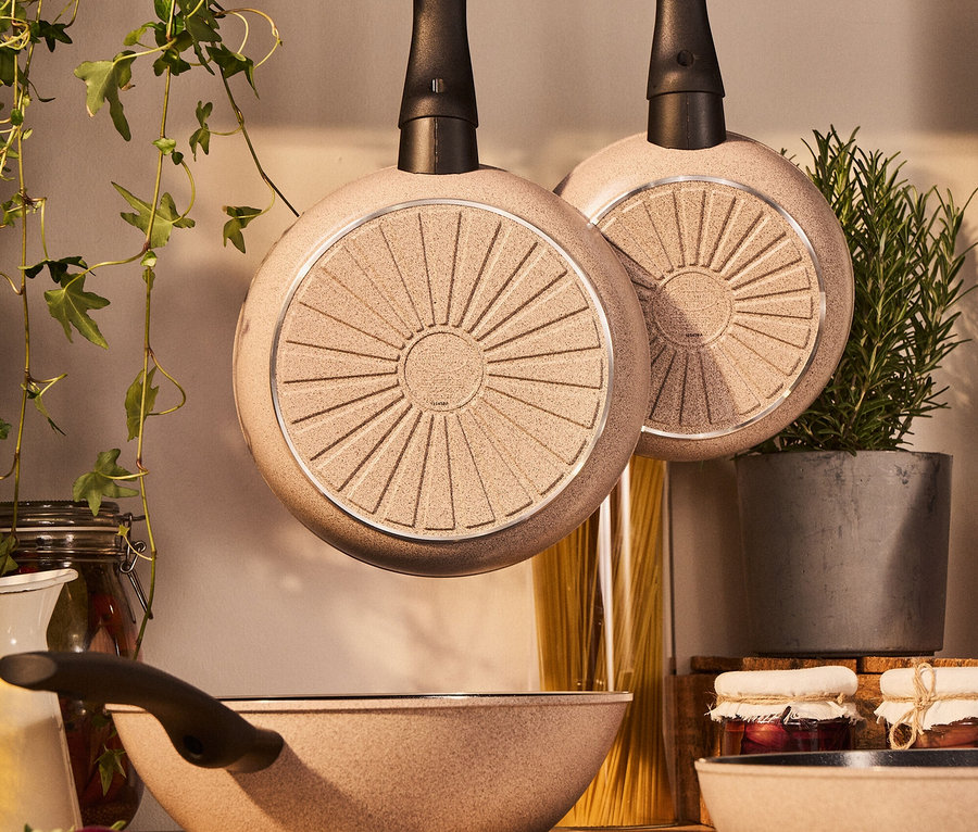 Zwei Pfannen hängen über einem Herd, darunter eine Pfanne auf einem Kochfeld.