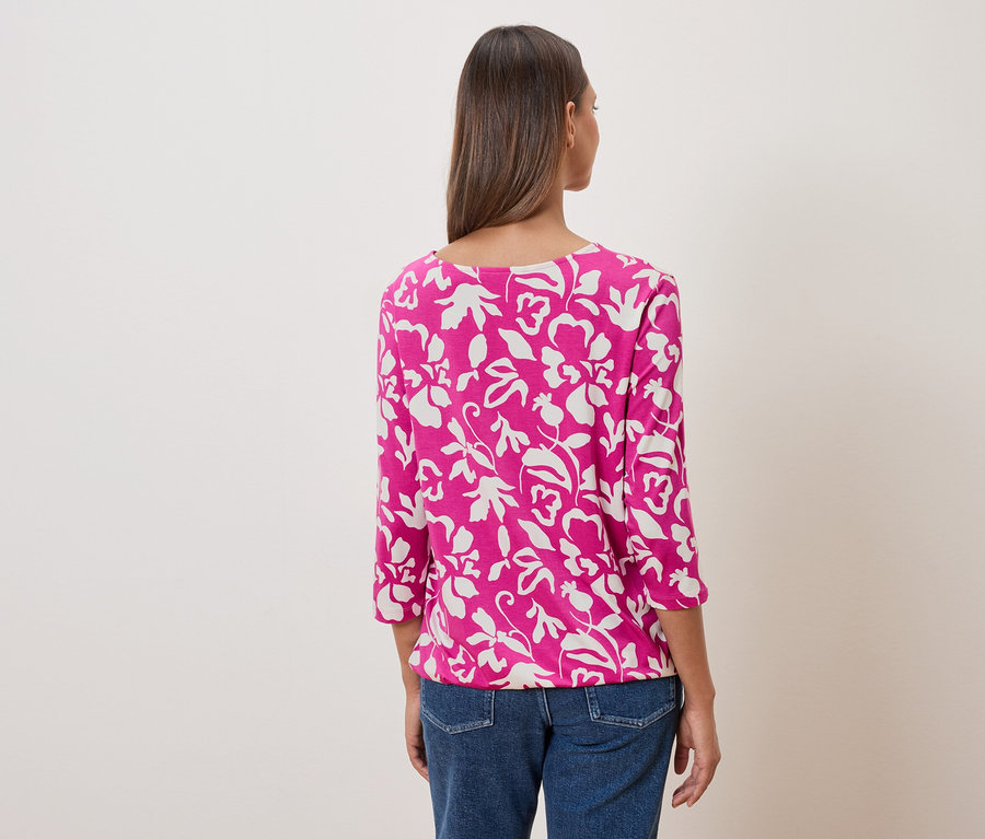 Rückansicht einer Frau mit einem pinkfarbenen Oberteil mit Blumendruck und Jeans.