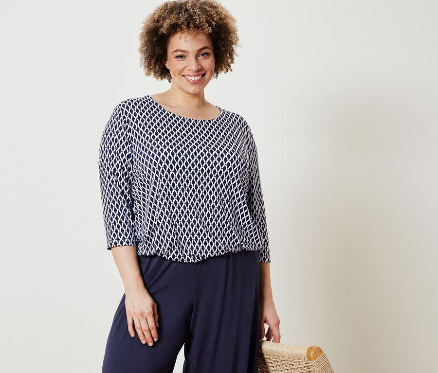 Frau posiert in bedrucktem Blusenshirt und dunkelblauer Palazzohose.