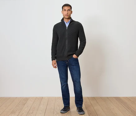 Mann steht und trägt eine Strickjacke, anthrazit meliert, dazu Jeans und Schuhe.
