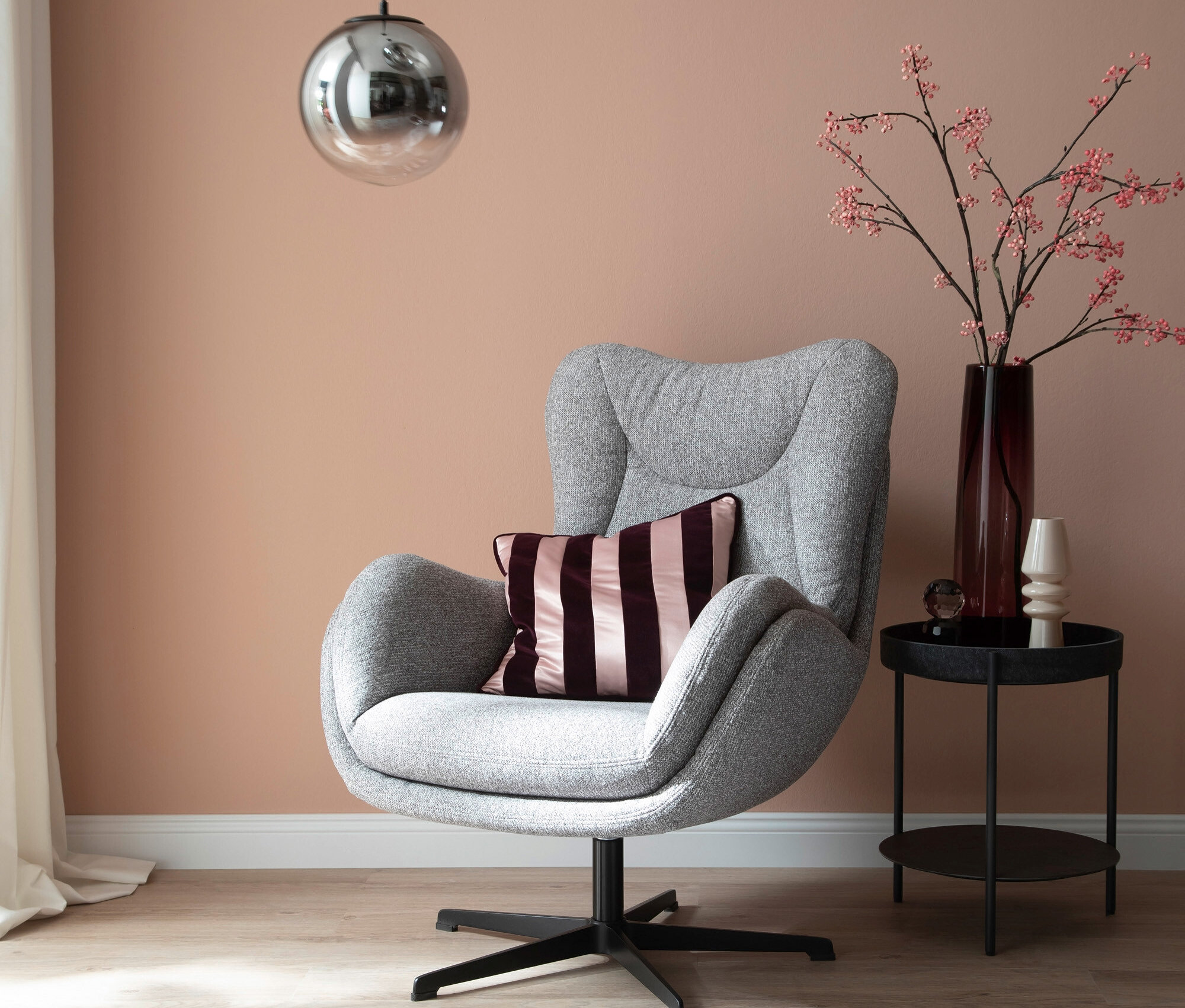 Ein grauer Sessel mit einem lila Kissen steht auf einem grauen Teppich neben einem Tisch mit einer Vase und Dekoration. Über dem Sessel hängen zwei silberne Lampen.