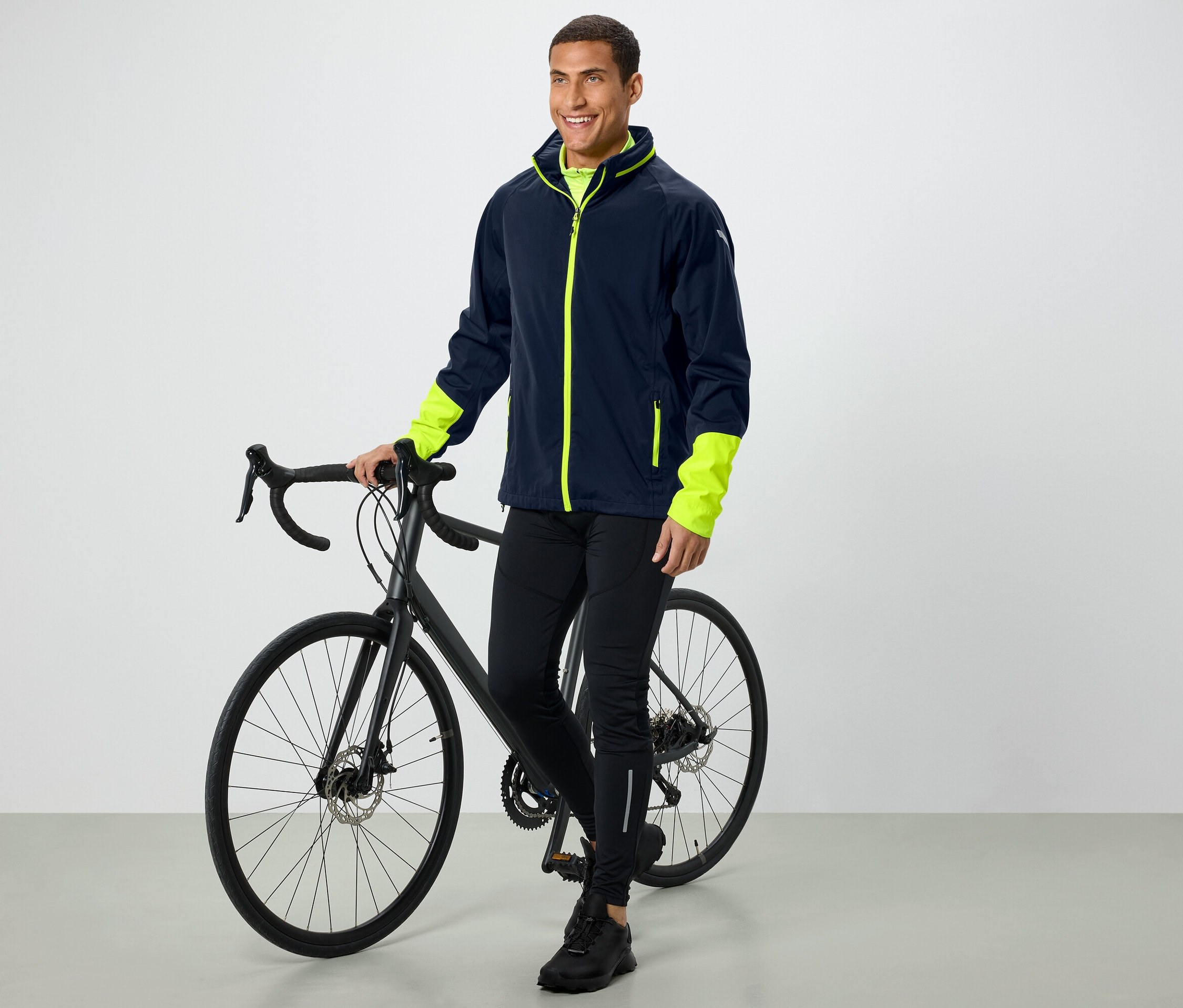 Ein Mann steht neben einem Fahrrad und trägt eine Jacke mit neonfarbenen Ärmeln.