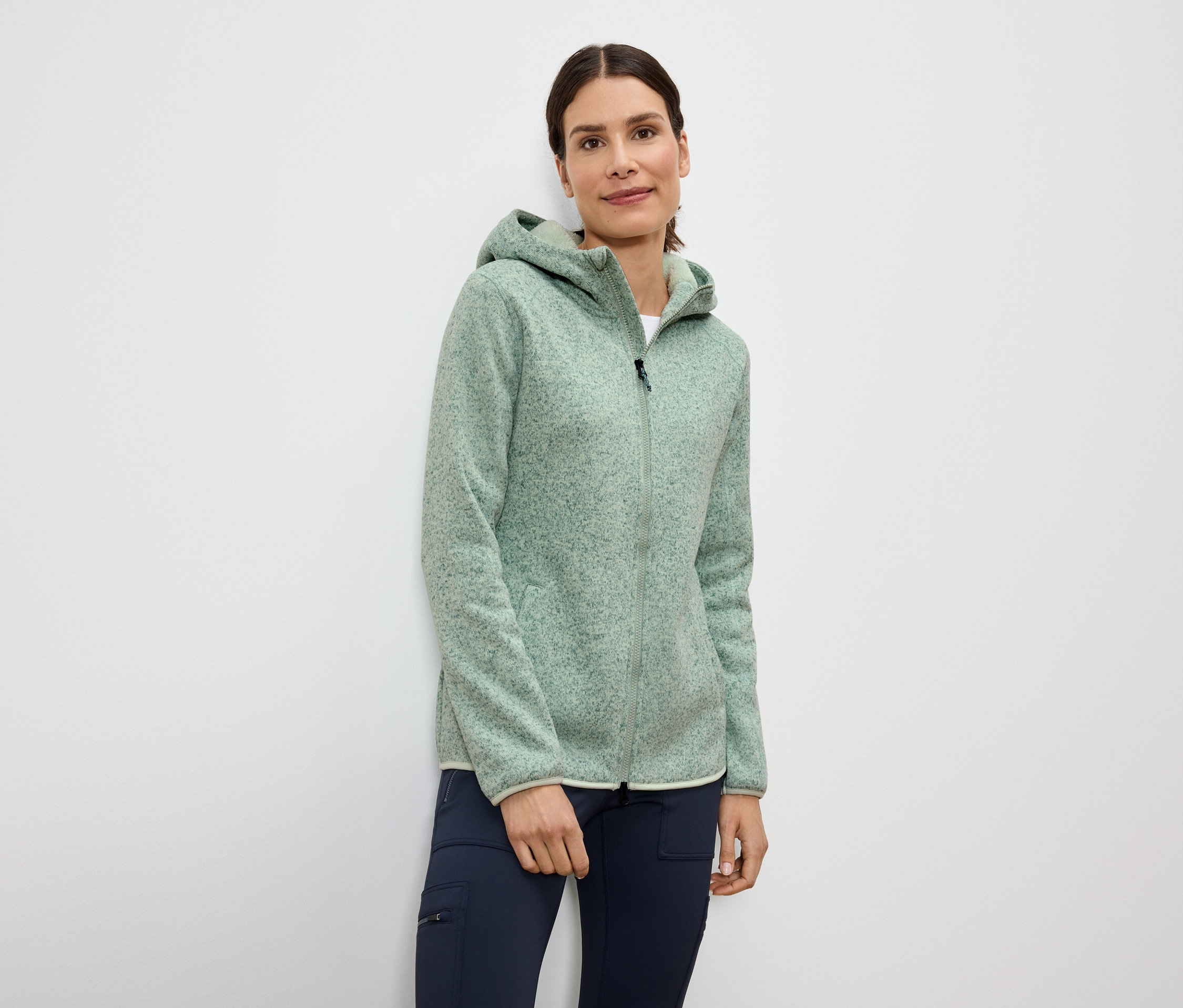 Frau trägt hellgrüne Fleecejacke mit Reißverschluss und Kapuze und dunkelblaue Hose.