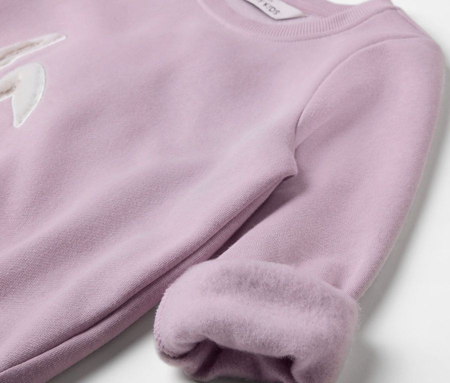 Detailaufnahme eines hellvioletten Sweatshirts mit Hasenapplikation und hochgekrempelten Ärmeln.