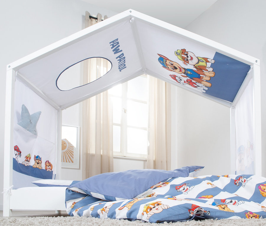 Ein weißes Kinderbett mit Paw Patrol-Motiv und blau-weißer Bettwäsche steht in einem hellen Raum.