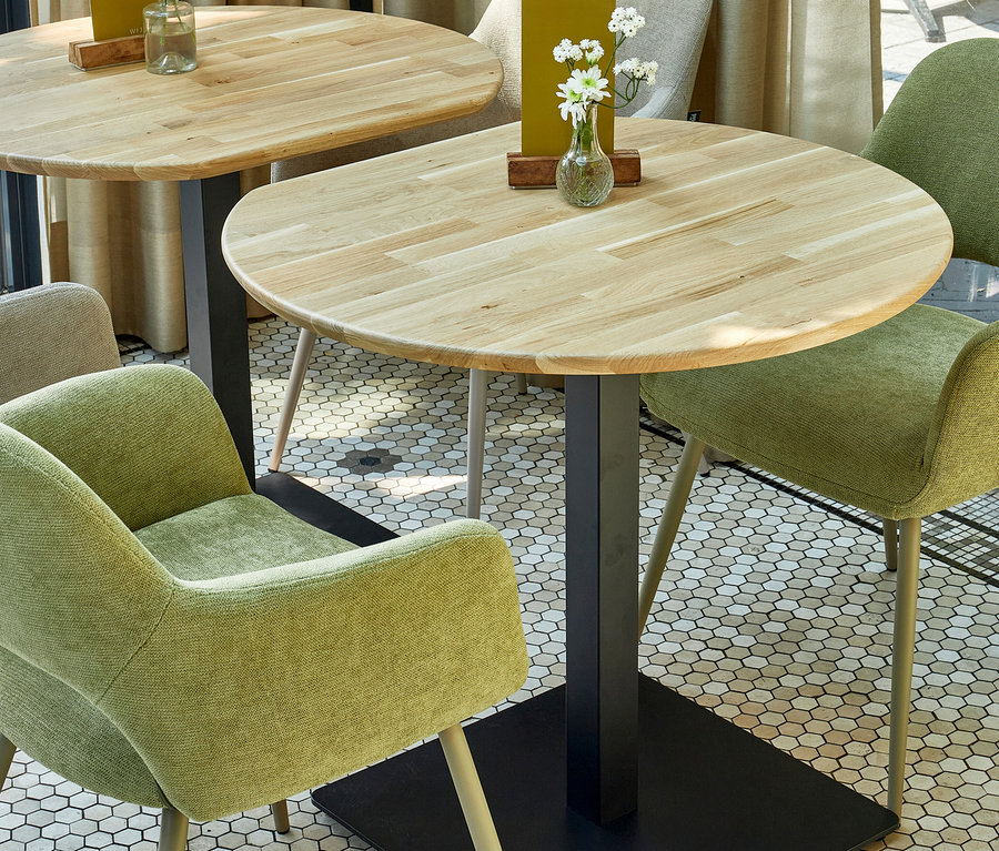 Zwei Tische mit Holzplatten und schwarzen Untergestellen. Auf den Tischen stehen Vasen mit weißen Blumen und gelbe Aufsteller. Um die Tische herum stehen grüne Stühle Woood »Jenny« 2er-Set, sage.