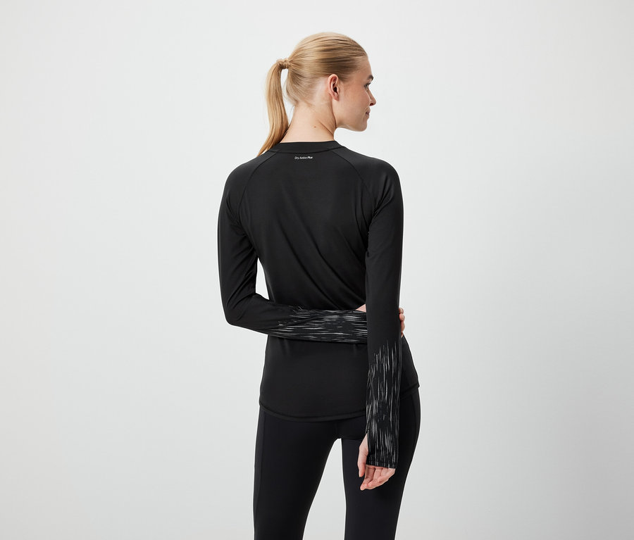 Blonde Frau mit Pferdeschwanz trägt schwarze Sportbekleidung, von hinten gesehen.