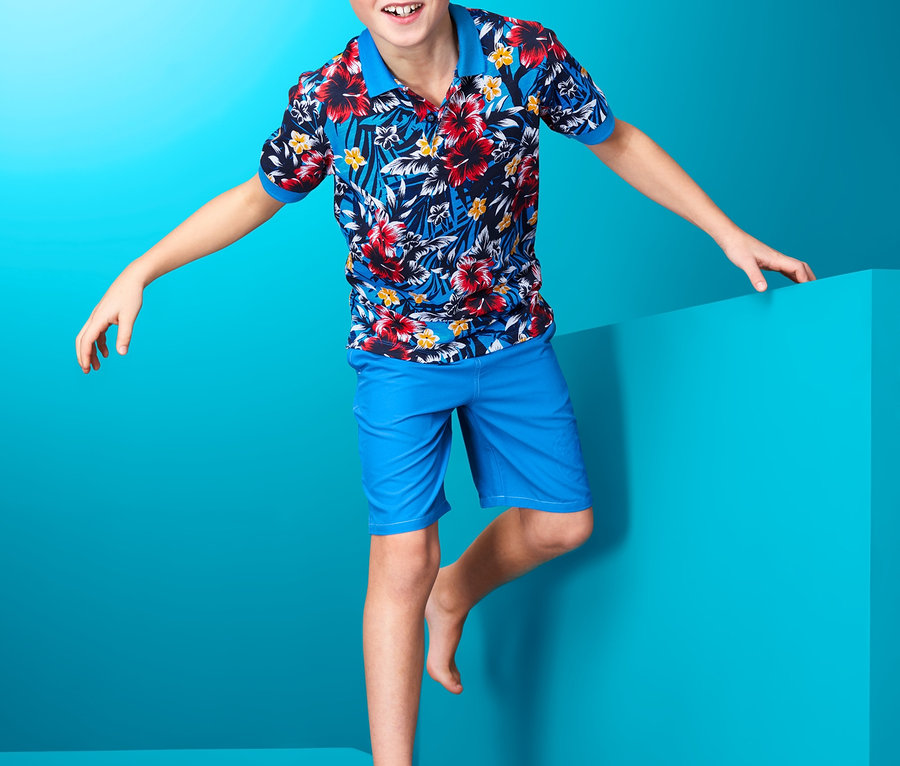 Junge posiert in Hawaii-Poloshirt und blauen Shorts.