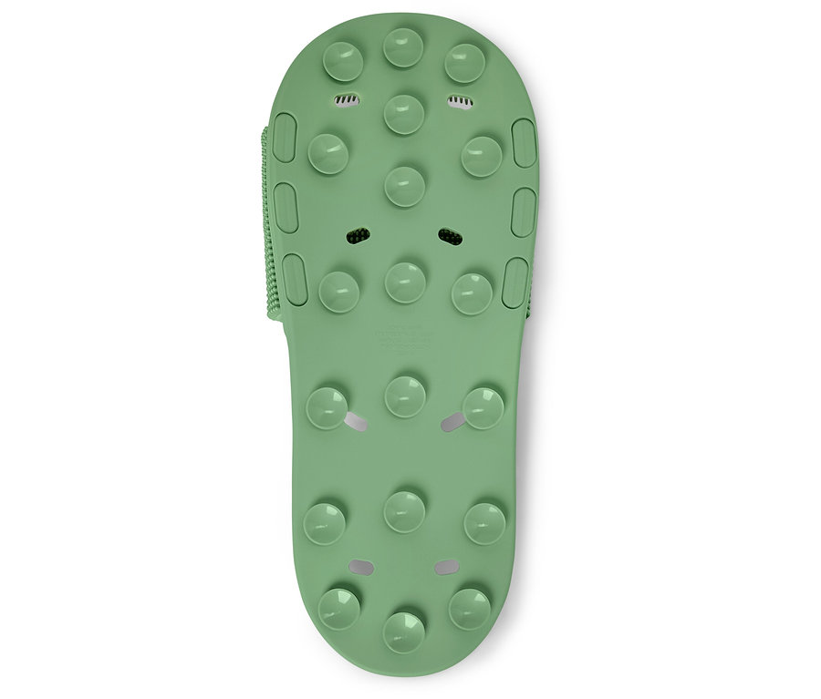 Nahaufnahme einer einzelnen grünen Badesandale mit Noppen auf weißem Grund.