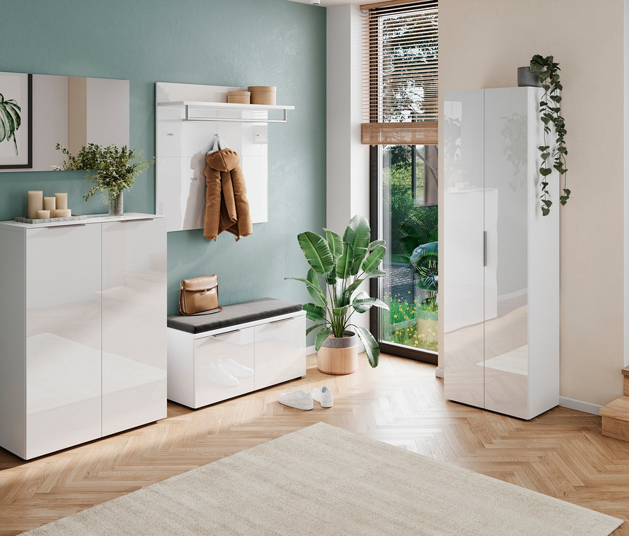 Eingangsbereich mit weißen Möbeln, darunter ein Schuhschrank, eine Bank mit grauem Kissen, ein Garderobenpaneel mit Jacke und eine Vitrine. Pflanzen dekorieren den Raum.