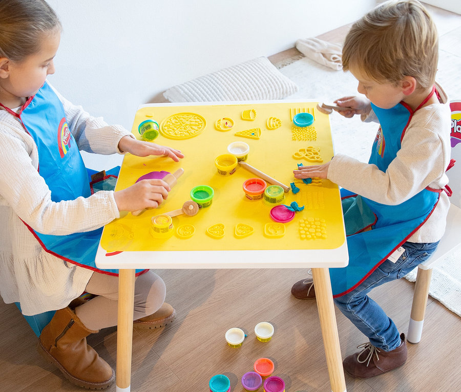 Zwei Kinder sitzen an einem gelben Tisch und spielen mit Knete. Auf dem Tisch liegen Förmchen und Werkzeuge.