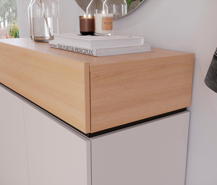 Auf einem weißen Schrank mit hellem Holzaufsatz stehen Kerzen, Bücher und eine Vase mit Pflanzen.