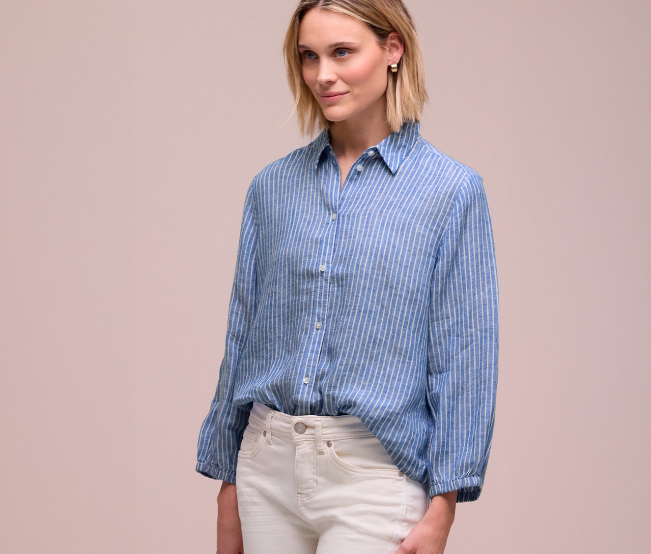 Frau mit blonden Haaren trägt ein blau-weiß gestreiftes Hemd und weiße Jeans.