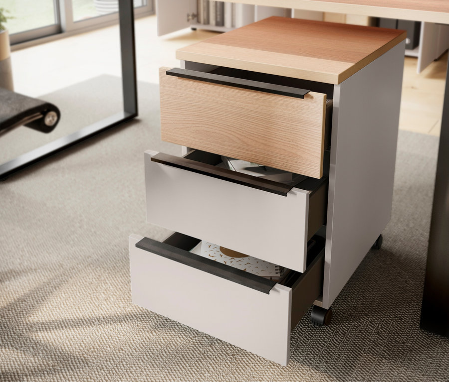 Ein Rollcontainer mit drei Schubladen, von denen zwei geöffnet sind, steht unter einem Schreibtisch.