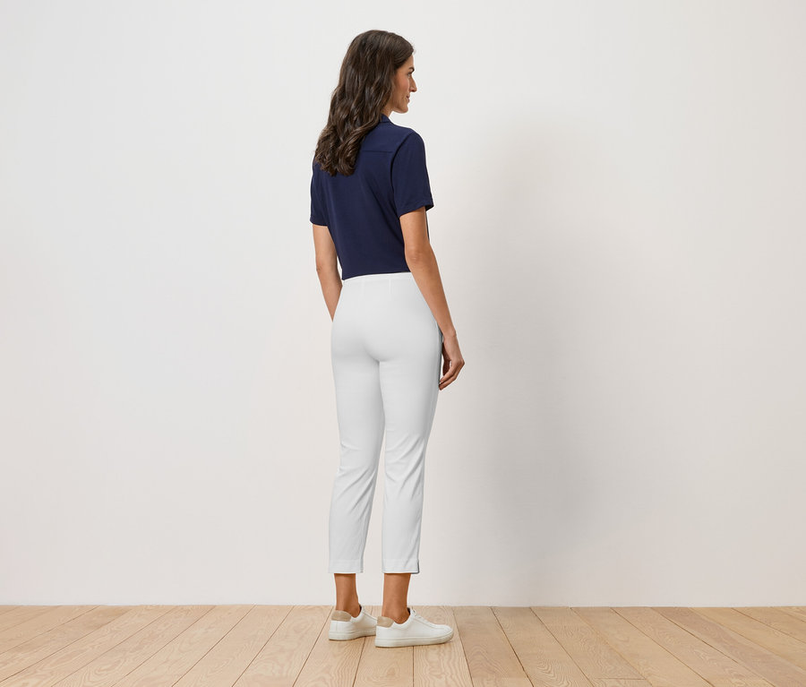 Eine Frau steht mit dem Rücken zur Kamera, sie trägt ein marineblaues Poloshirt, eine weiße Hose und weiße Schuhe.