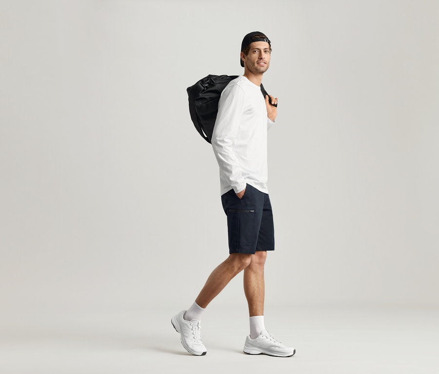 Mann geht mit schwarzer Tasche über der Schulter und trägt ein 2 Langarmshirts.