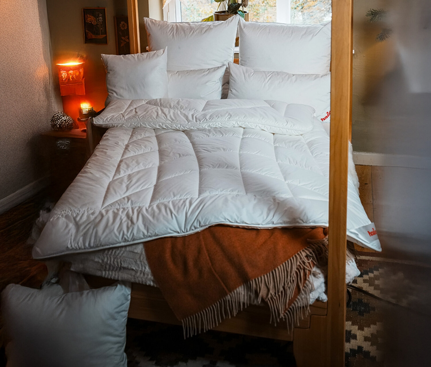 Bett mit weißer »ElbTraum« Winter-Faserdecke von Paradies, Normalgröße, mehreren Kissen und einer orangefarbenen Decke.