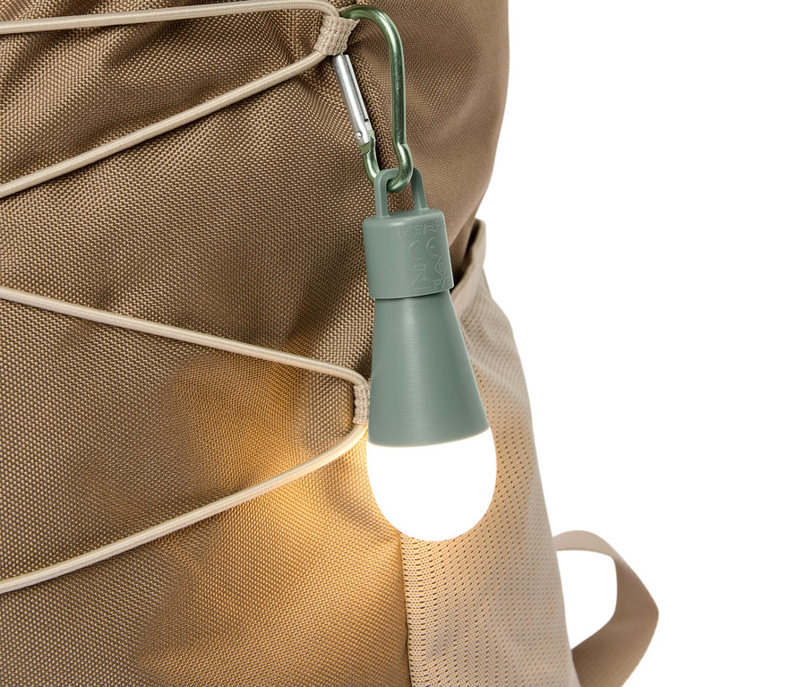 Nahaufnahme eines olivgrünen LED-Lichts, das mit einem Karabiner an einem beigen Rucksack befestigt ist.