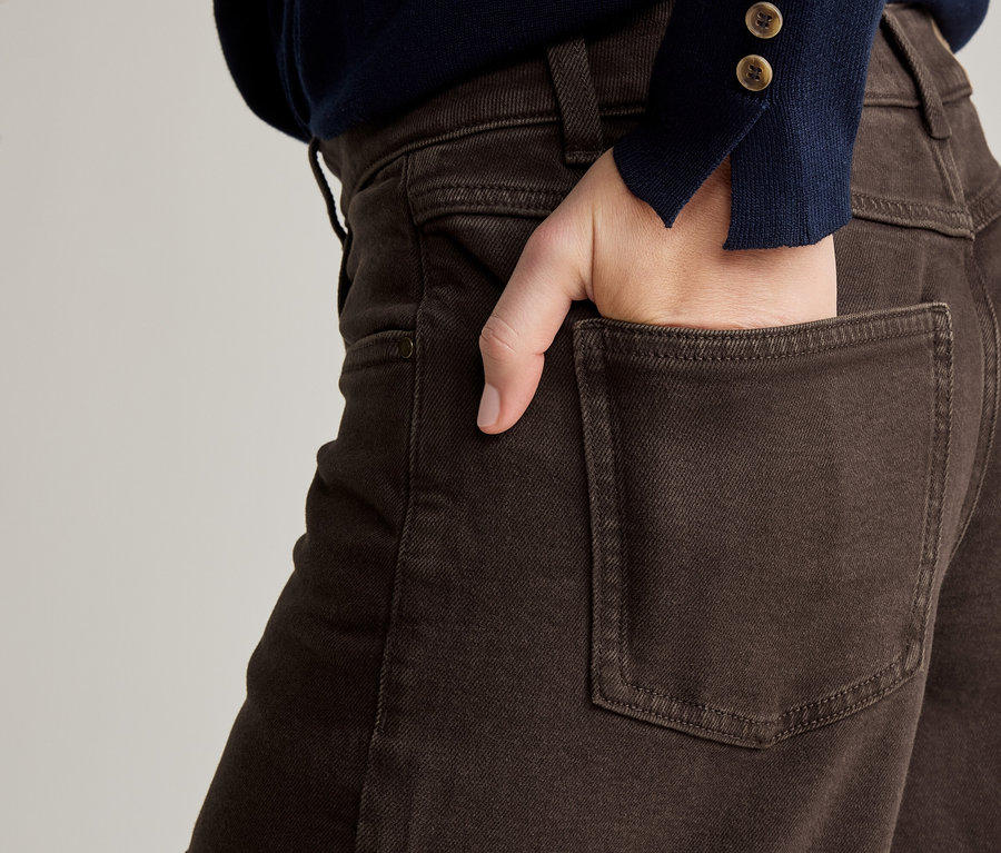Nahaufnahme einer Person mit einer Hand in der Gesäßtasche einer braunen Hose und einem marineblauen Pullover.