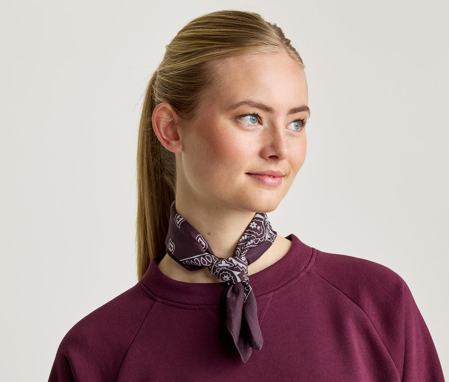 Frau mit blondem Haar trägt ein dunkelrotes Sweatshirt und ein gemustertes Halstuch.