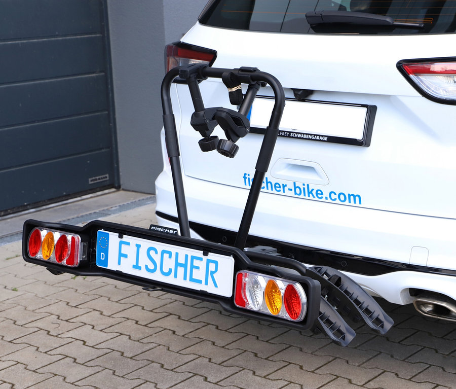 Schwarzer Kupplungs-Fahrradträger »SmartLine black« am Heck eines weißen Autos, mit Kennzeichenhalter und Rückleuchten, vor einer dunklen Garagentür.