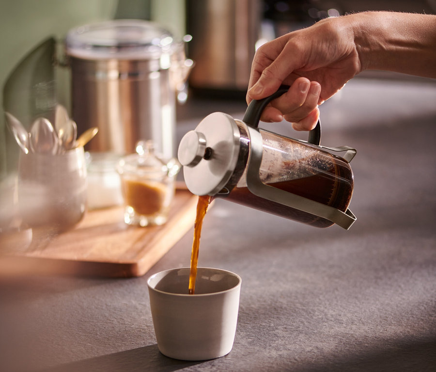 Eine Hand gießt Kaffee aus einer silbernen Siebstempelkanne 300 ml in eine Tasse.