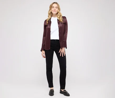 Eine Frau mit blonden Haaren steht lächelnd vor weißem Hintergrund. Sie trägt ein weißes T-Shirt, ein offenes weinrotes Hemd, schwarze Skinny Jeans und schwarze Loafer mit goldenen Schnallen.