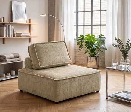 Beiger, modularer Sessel mit Kissen in einem Wohnzimmer mit Holzregalen, einer Monstera-Pflanze, einer Stehlampe und einem Glastisch.