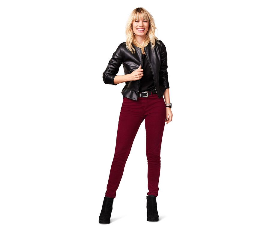 Eine lächelnde Frau posiert in einer schwarzen Lederjacke und bordeauxfarbenen Jeggings.