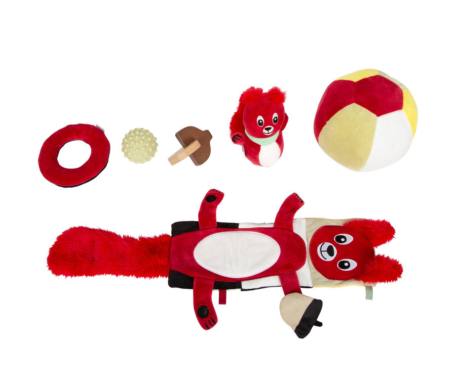 Eine rote Eichhörnchen-Spielmatte mit Eichel, ein roter Plüschring, ein gelber Strukturball, ein Holzpilz, ein kleines rotes Plüsch-Eichhörnchen und ein rot-gelb-weißer Plüschball, alles Babyspielzeug, auf weißem Hintergrund.