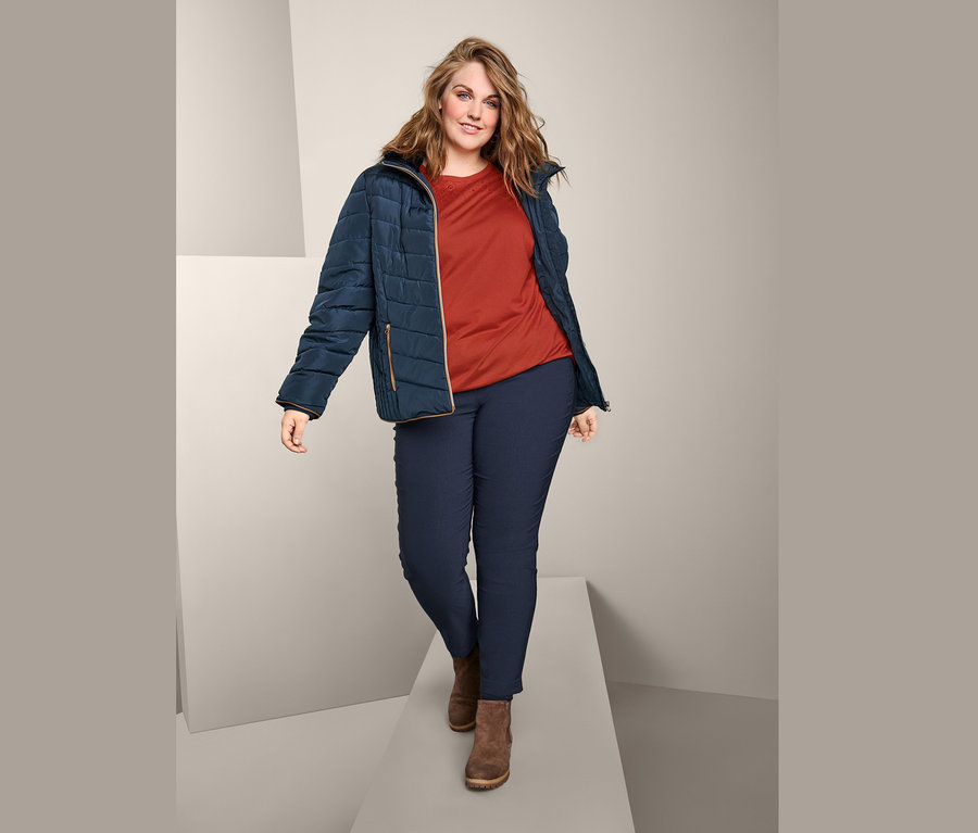 Eine Frau geht auf einem Laufsteg und trägt eine Steppjacke, ein Kurzarmshirt mit Stickerei und eine Bengalin-Hose.