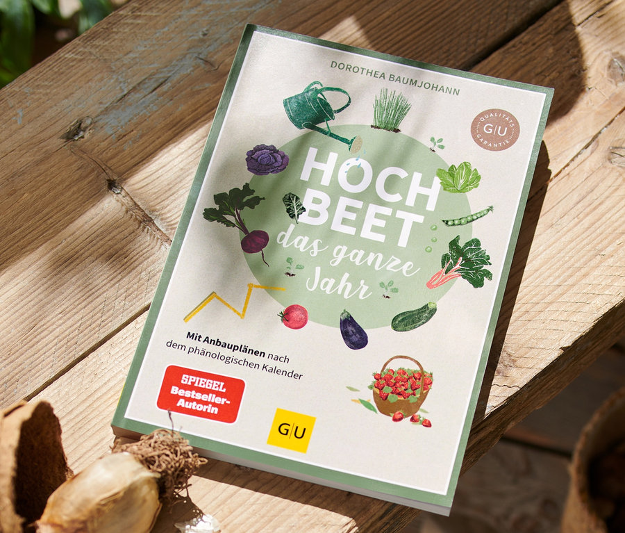 Buch »Hochbeet – das ganze Jahr« liegt auf Holztisch neben Blumentopf.