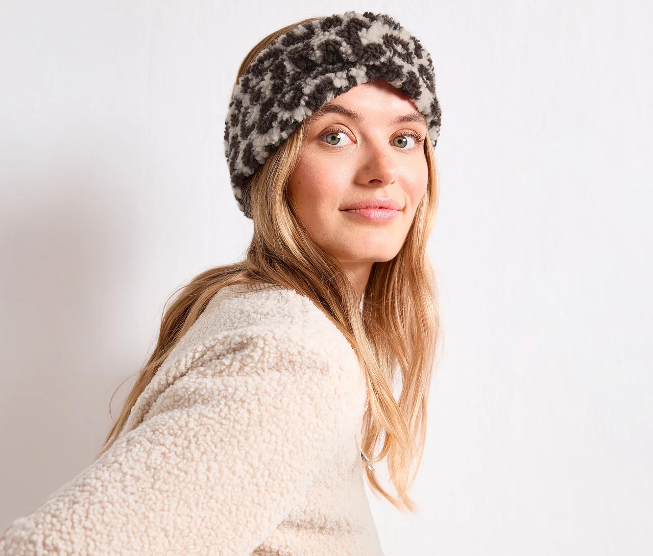Frau mit langen blonden Haaren trägt ein Street One Stirnband mit dunkelgrauem Leopardenmuster und einen cremefarbenen Teddyfellpullover.