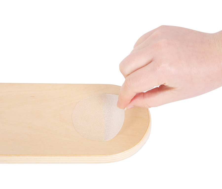 Eine Hand platziert einen kleinen small foot Balancierstein »Adventure« auf einem Holzbrett.