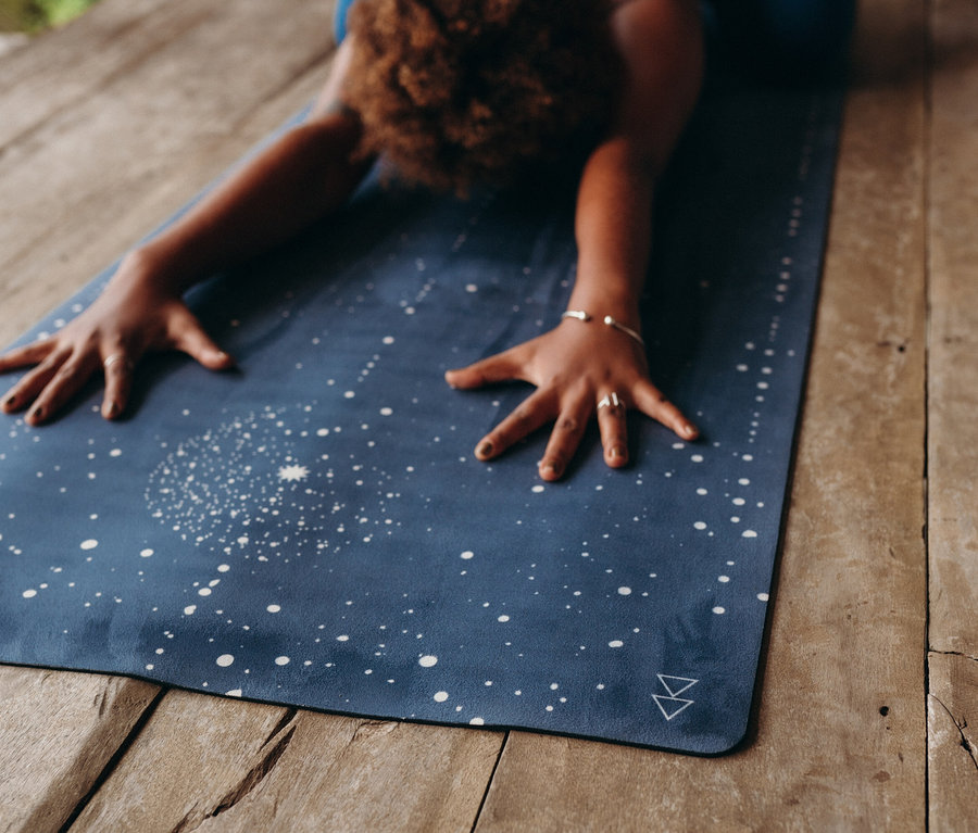Frau dehnt sich auf blauer Yogamatte mit weißen Sternen auf Holzboden.