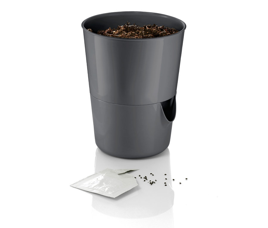 Grauer Kräutertopf mit Bewässerungssystem, Erde und Samen auf weißem Hintergrund.