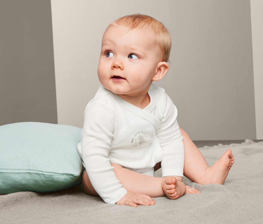 Sitzendes Baby trägt einen 5er Pack Baumwoll-Langarmbody.