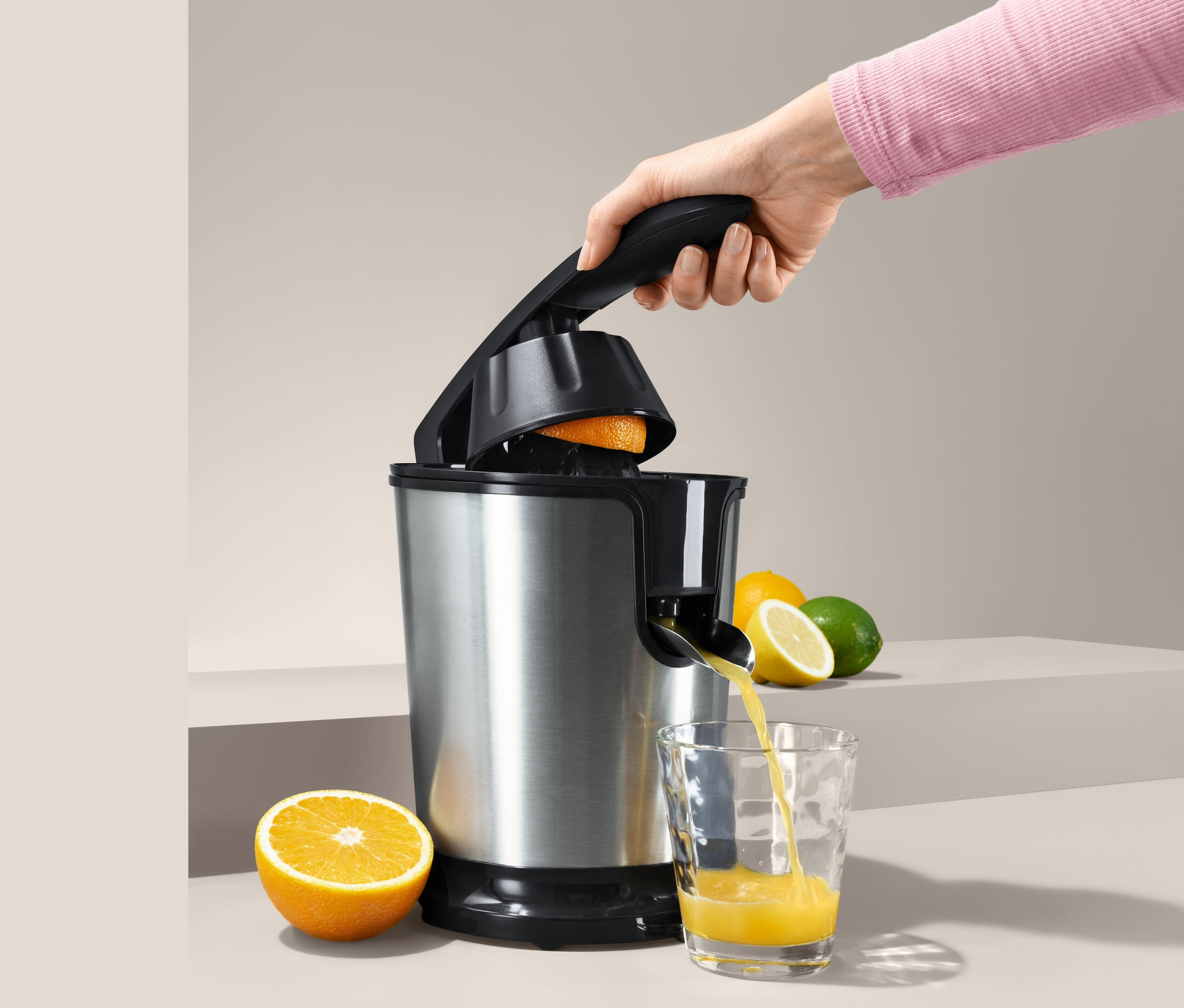 Hand presst Orange in elektrischer Orangenpresse, Saft fließt in Glas.