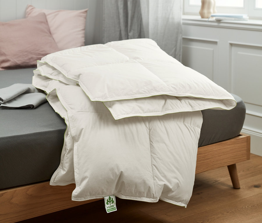 Ein gefaltetes irisette® greenline Daunen-Kassettenbett liegt auf einem Bett.