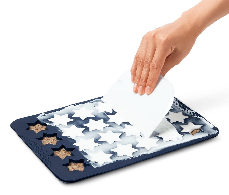 Eine Hand verteilt Teig auf einer Zimtstern-Backmatte.