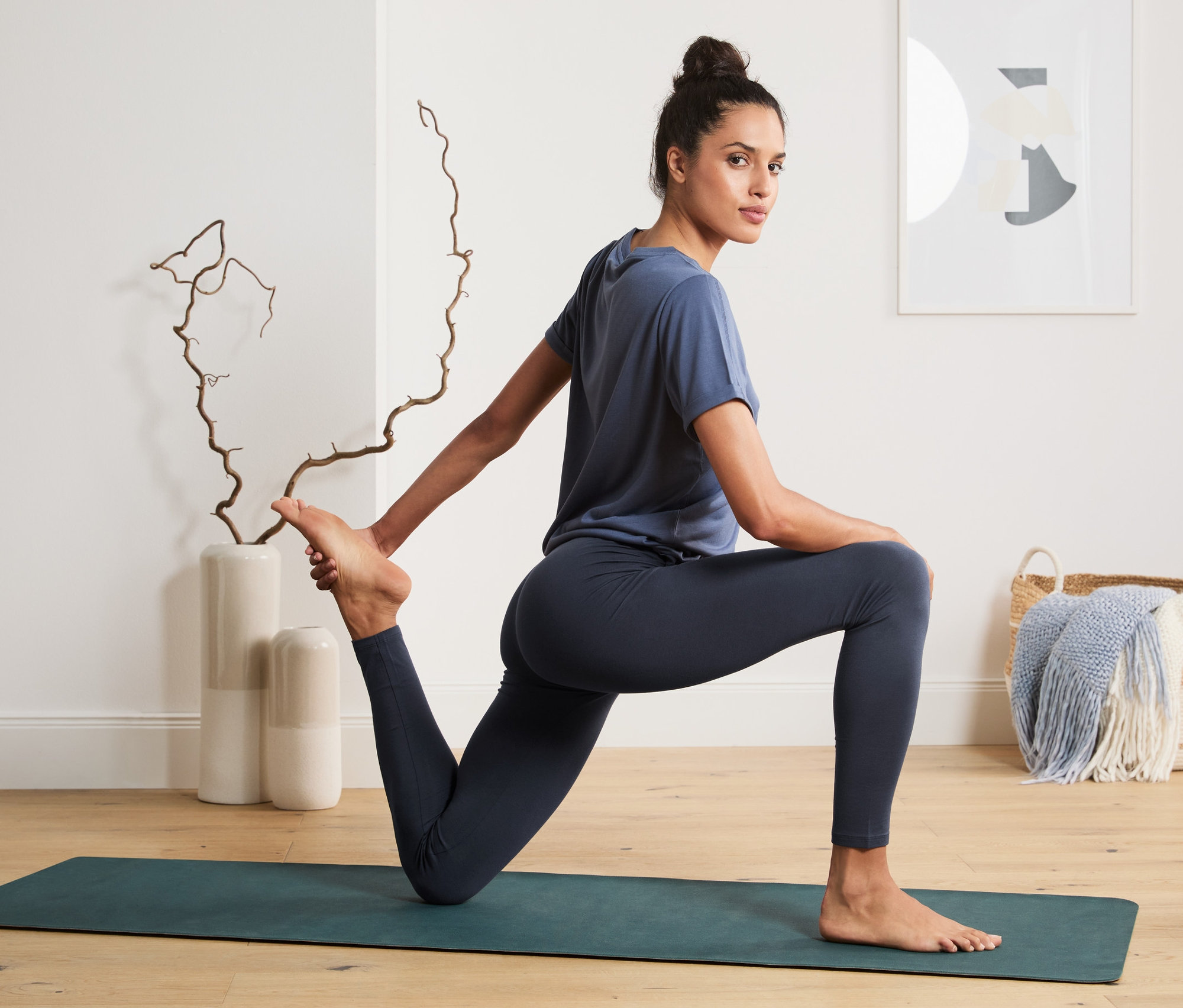 Frau in blauer Sportbekleidung dehnt sich auf einer Matte. Sie trägt eine Sporttight.