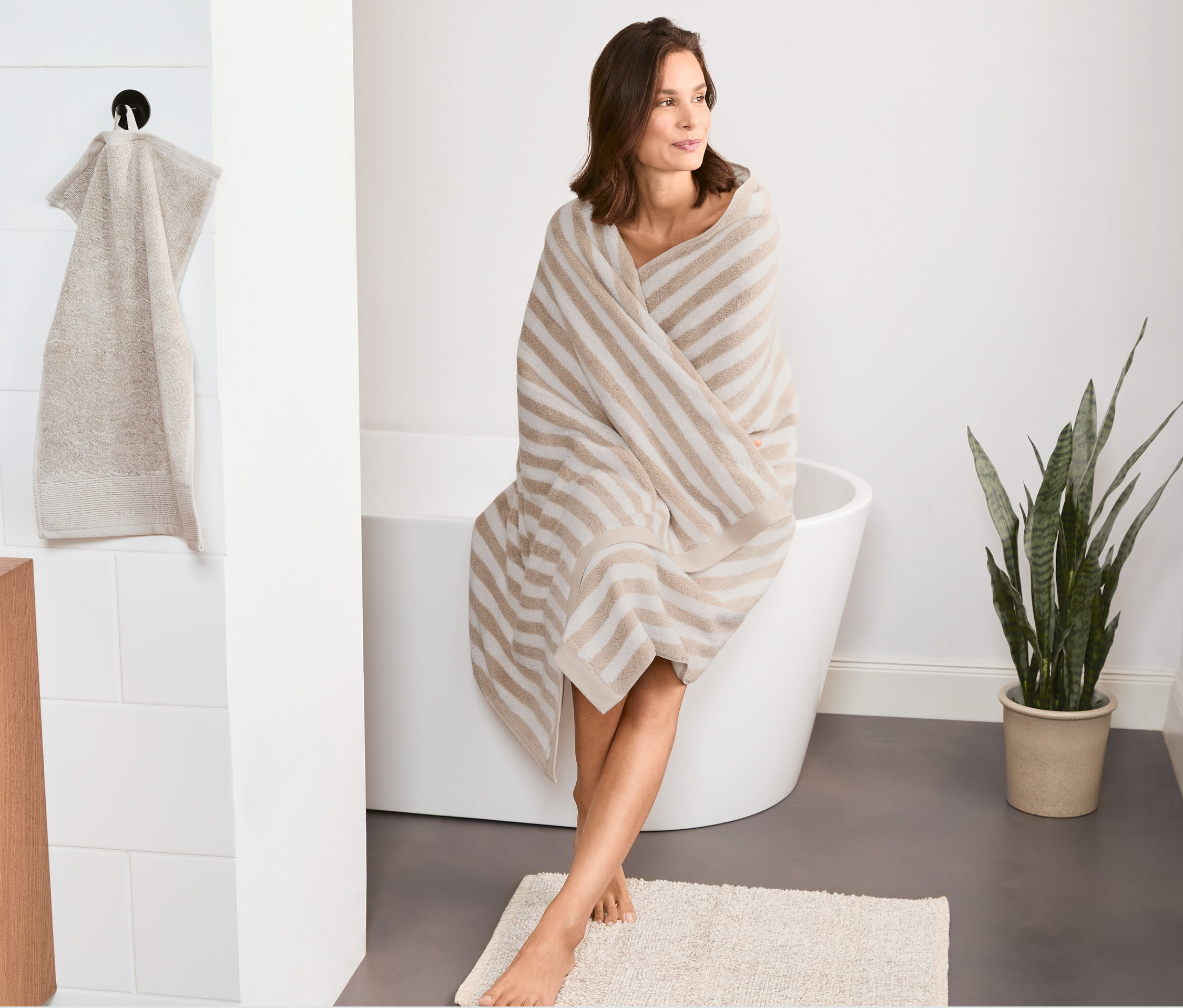 Frau sitzt mit Premium Badetuch XL umwickelt auf Badewannenrand.