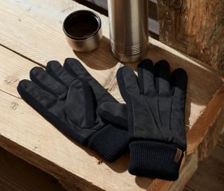 Auf einer Holzbank liegen Handschuhe, eine Thermoskanne und ein offener Becher.