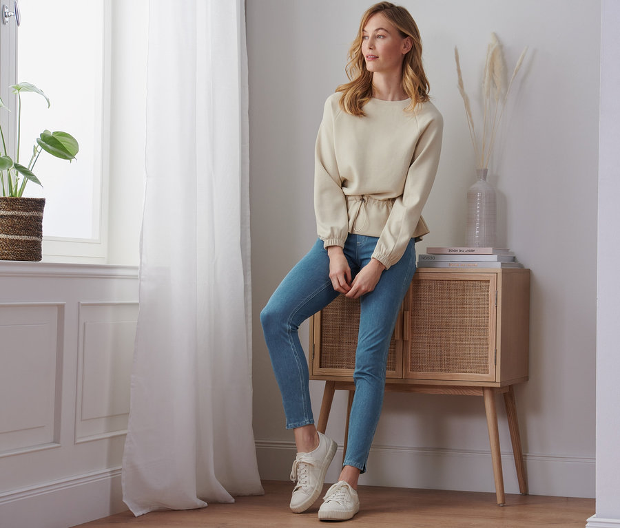 Frau sitzt an einer Kommode und trägt Jeggings.
