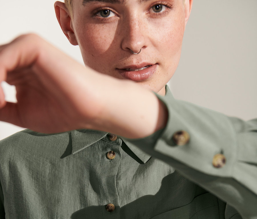 Frau verdeckt ihr Gesicht mit der Hand und trägt eine Hemdbluse.