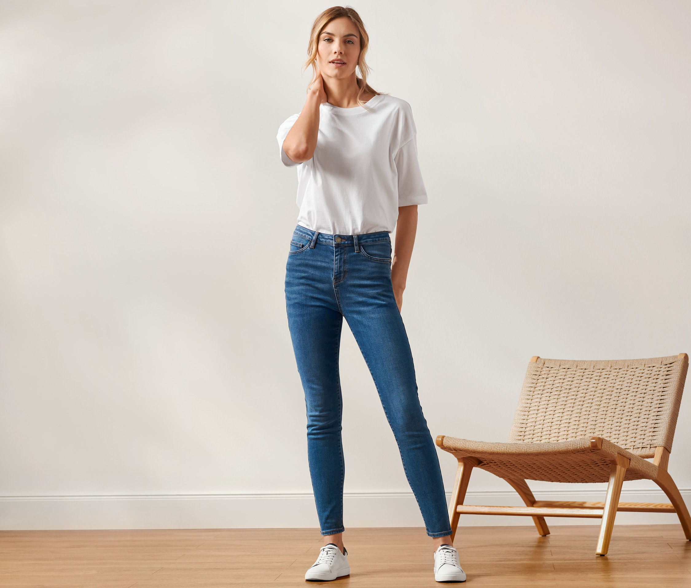 Frau posiert in Skinny-Denim »Fit Hanna«, weißem T-Shirt und Turnschuhen.