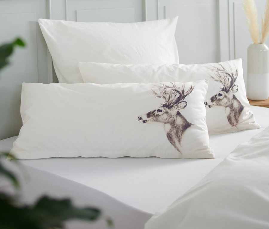 Auf einem Bett liegen zwei Perkal-Kopfkissenbezüge, eines davon mit Hirschmotiv.