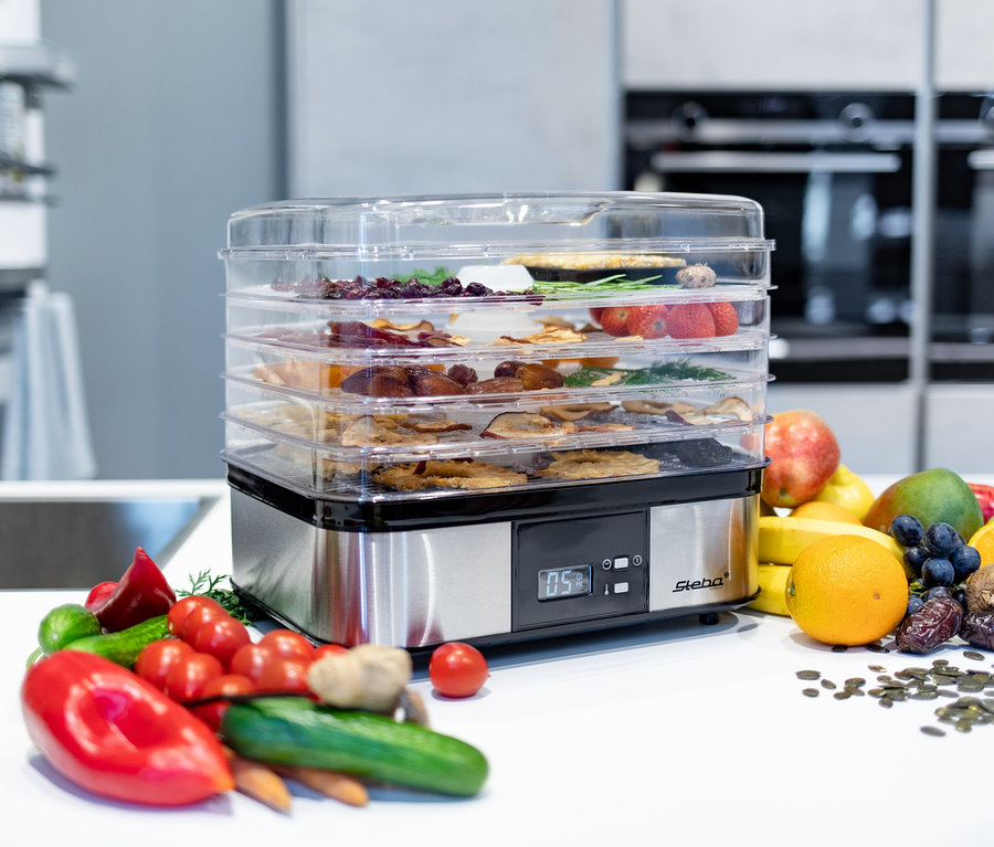 Mehrschichtiger Steba-Dörrautomat ED 5 voll mit getrocknetem Obst und Gemüse auf einer weißen Theke mit frischem Obst und Gemüse.