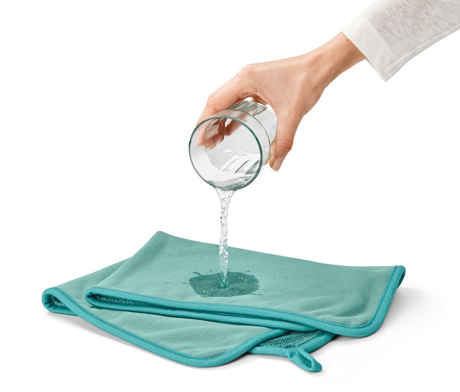 Hand gießt Wasser aus einem Glas auf ein blaugrünes, saugstarkes Trockentuch.