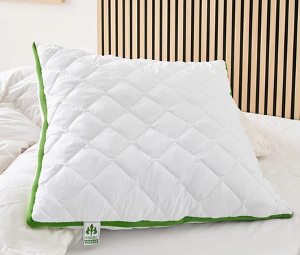 Ein weißes, gestepptes irisette® greenline Kopfkissen mit Klimaband und grüner Bordüre liegt auf einem Bett.